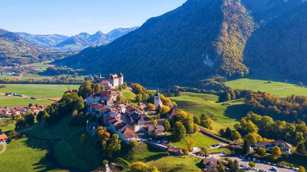 Aerial view of Gruyères village and medieval castle surrounded by green hills and mountains in Switzerland