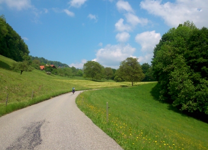 Cyclist on a scenic countryside road near Geneva surrounded by green hills and blue sky