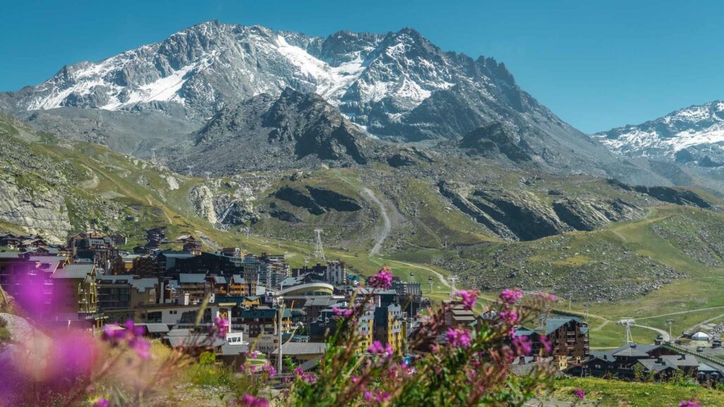 Val Thorens village in the French Alps with snow-capped mountains and purple wildflowers.